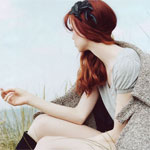Аватар Рыжеволосая девушка, с черным украшение в волосах, с пальто на плечах, сидит и смотрит на море в профиль